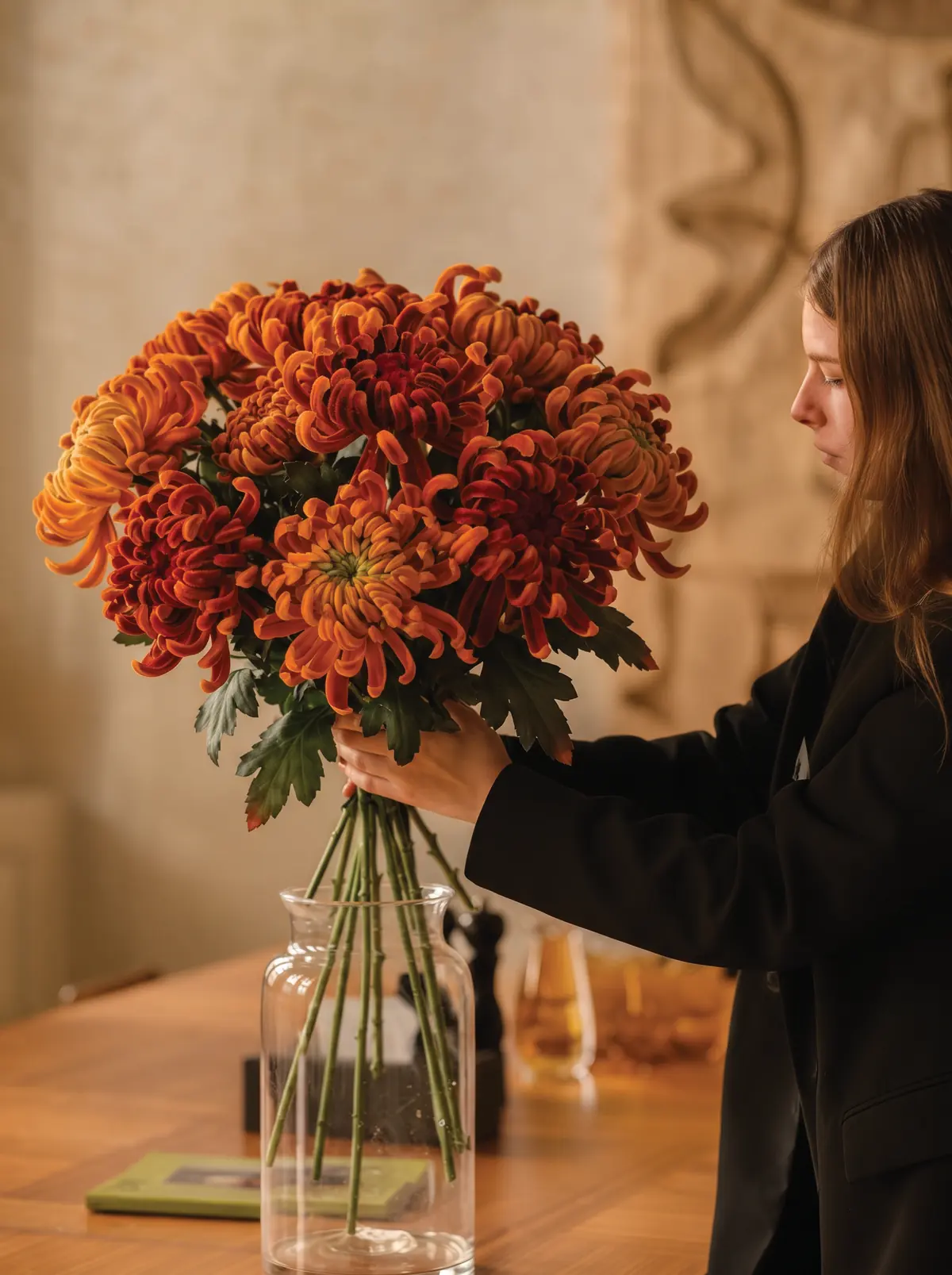 A florist arranging a large bouquet of orange chrysanthemums in a glass vase