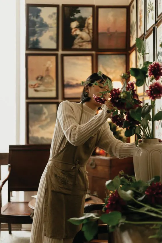 A florist arranging flowers in a room hung with framed paintings