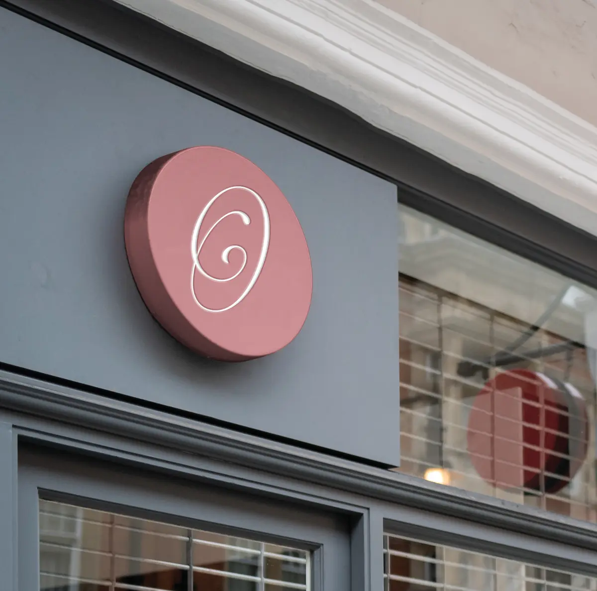 A round blush sign with the Felores monogram O on a grey shopfront