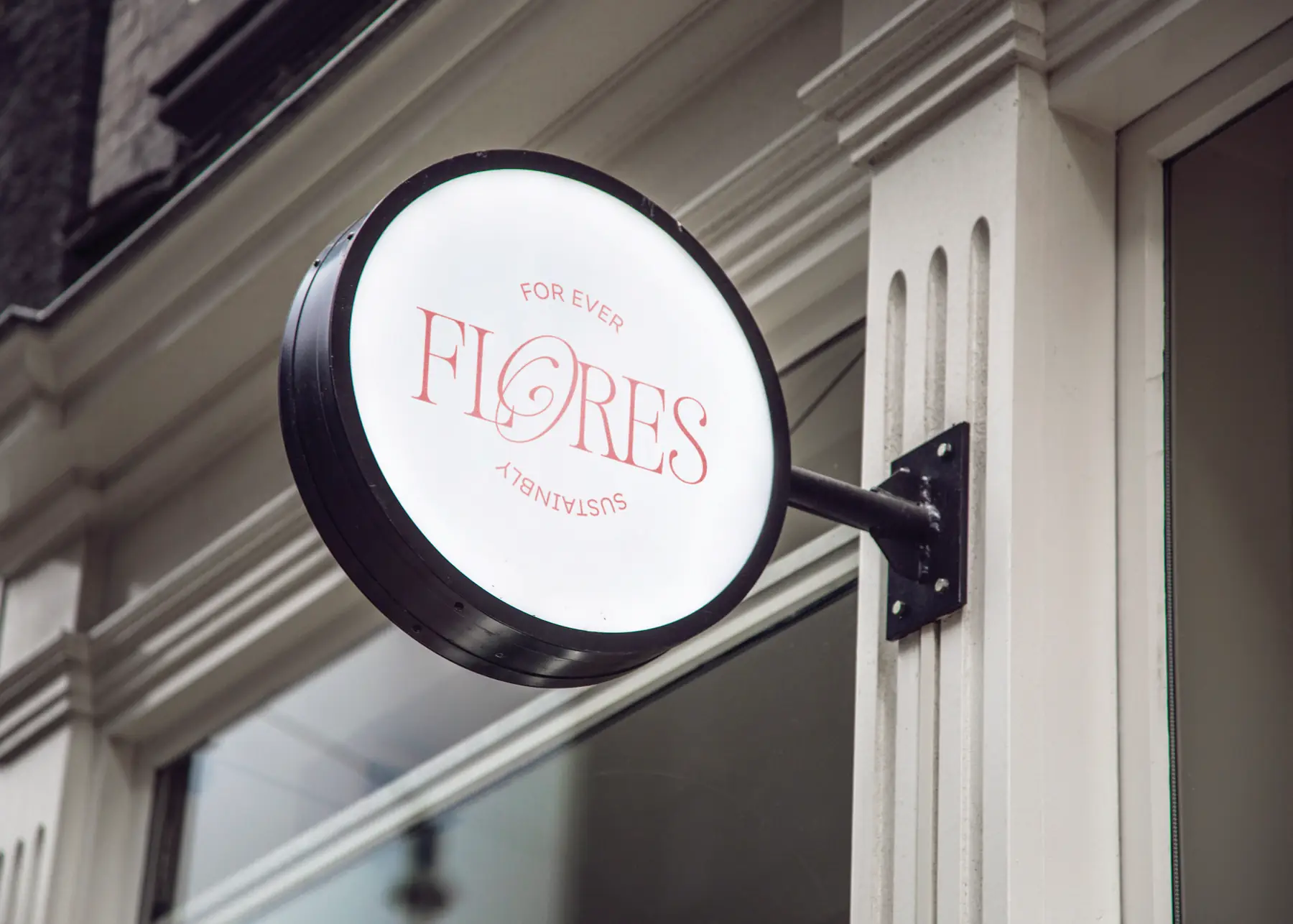 A round illuminated Felores shop sign hanging from a white facade
